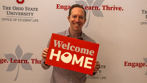 Person holding a sign that says Welcome Home with the O in the shape of a Buckeye