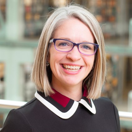 A headshot of Amanda L. Folk wearing purple glasses and a black blouse