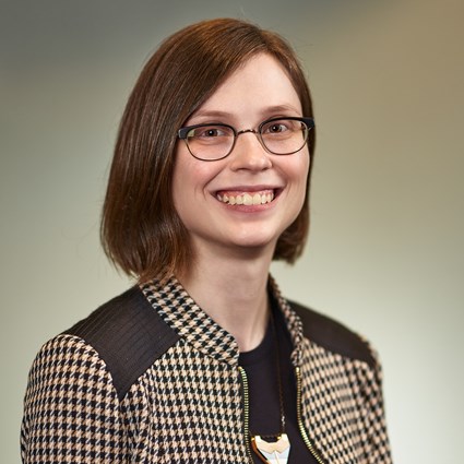 Headshot of Katie Dean in a black and beige patterned jacket and black shirt.