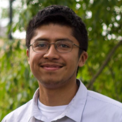 A headshot of Antonio D. Hernandez wearing glasses and a gray button up shirt