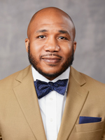 Headshot of Scott Graves wearing a tan suit with a blue bow tie
