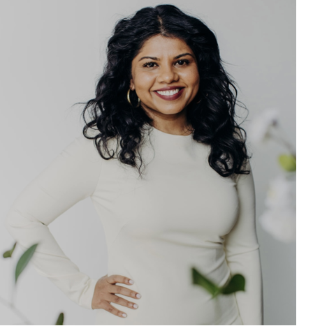 Woman in elegant white sweater dress with her hand on her hip smiling at the camera.