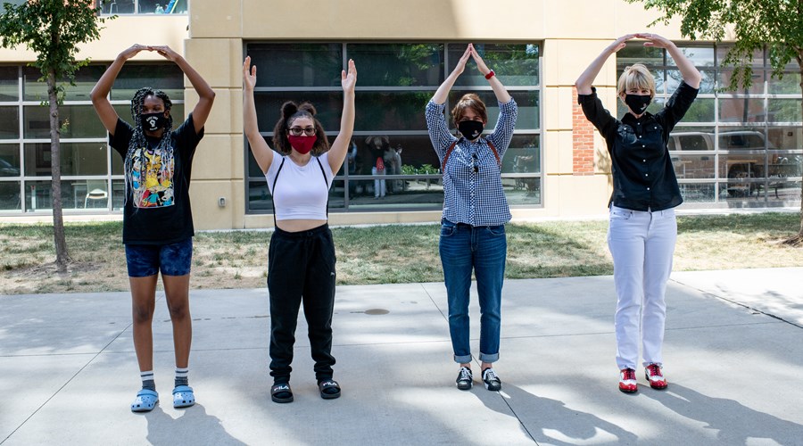 Three students and President Kristina M. Johnson wearing masks and spelling O-H-I-O