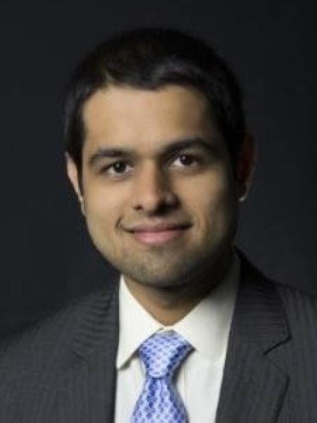Headshot of Adithya Jayakumar wearing a gray suit and blue tie.