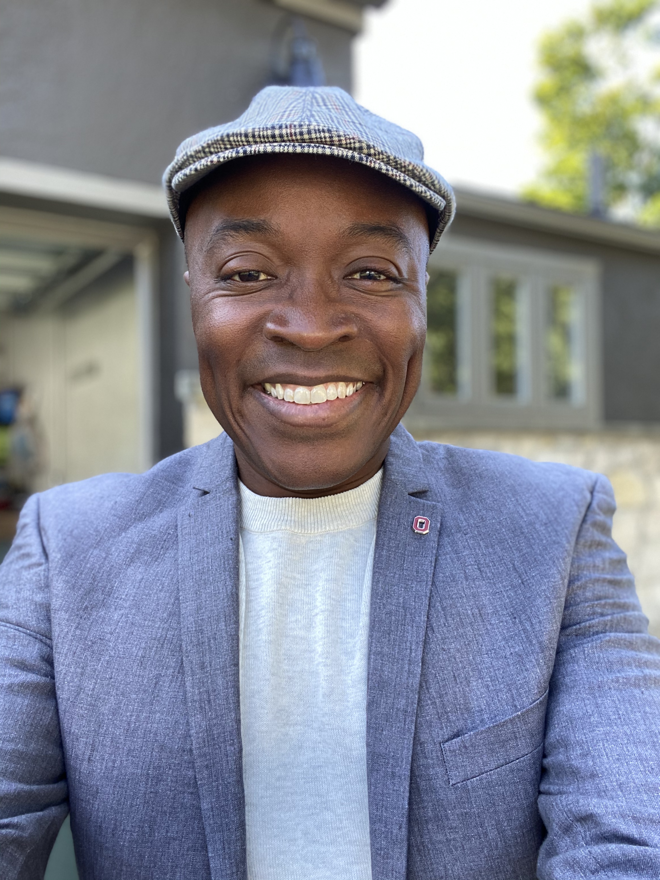 Headshot of Stephen Quaye smiling and wearing a plaid hat and blue-gray suit