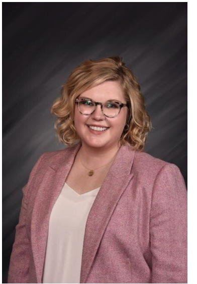 Woman wearing glasses and a soft pink blazer smiling at camera.