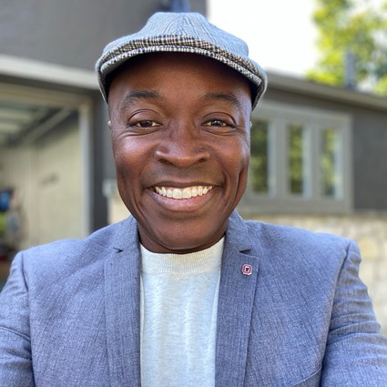 Headshot of Stephen Quaye wearing a gray blazer, a patterned hat, and a white shirt.