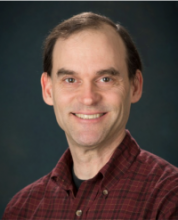 Headshot of Ted Clark wearing a red plaid shirt and smiling