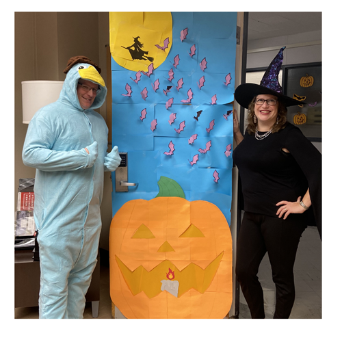 Katie Stanutz and another staff member wearing Halloween costumes standing next to a decorated door.